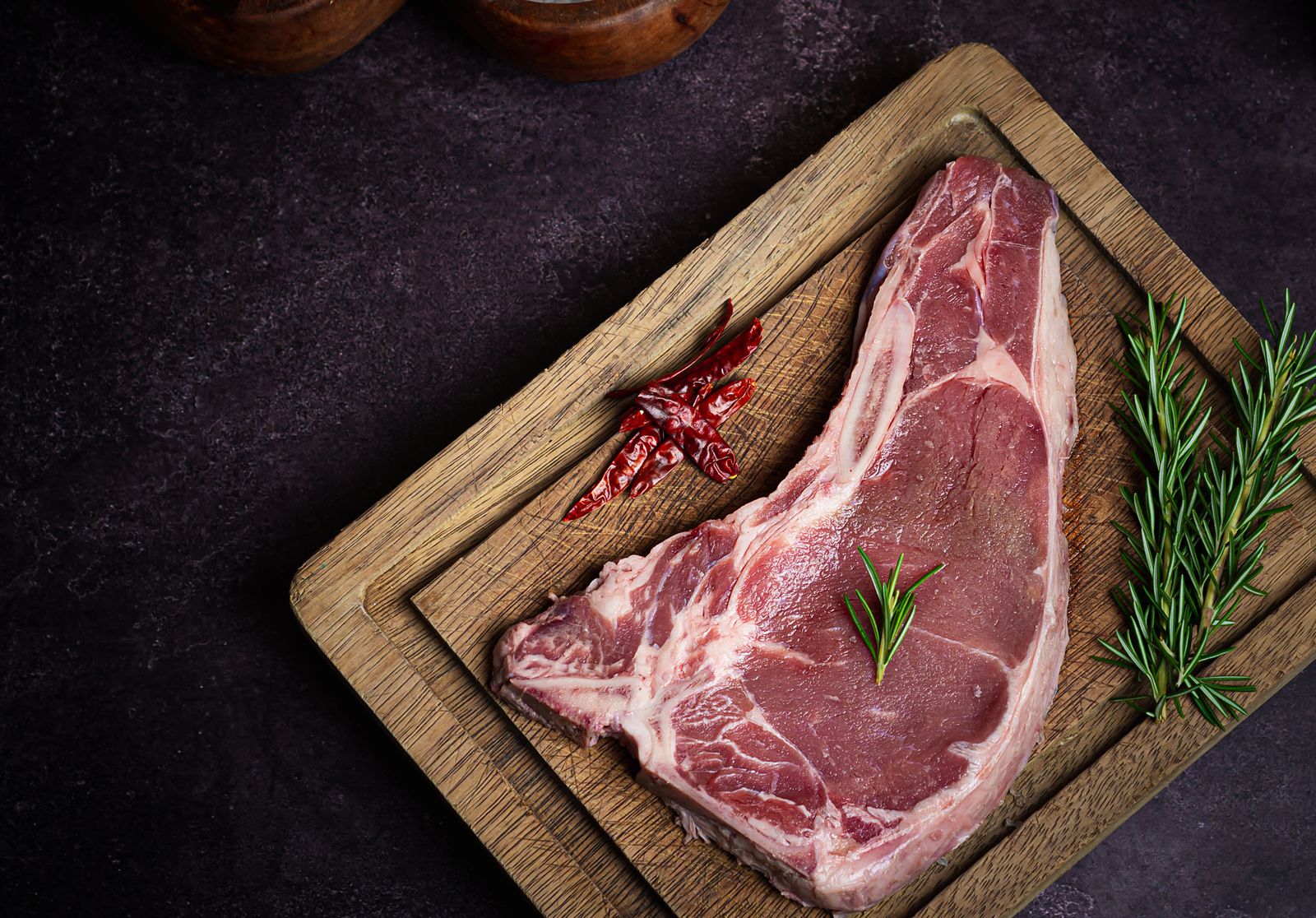 Pièce de bœuf crue sur planche avec romarin et poivre, avant taille en portions